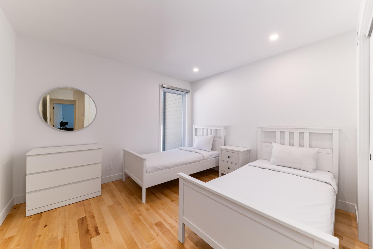 Chambre lumineuse avec deux lits simples, murs blancs et décor minimaliste.