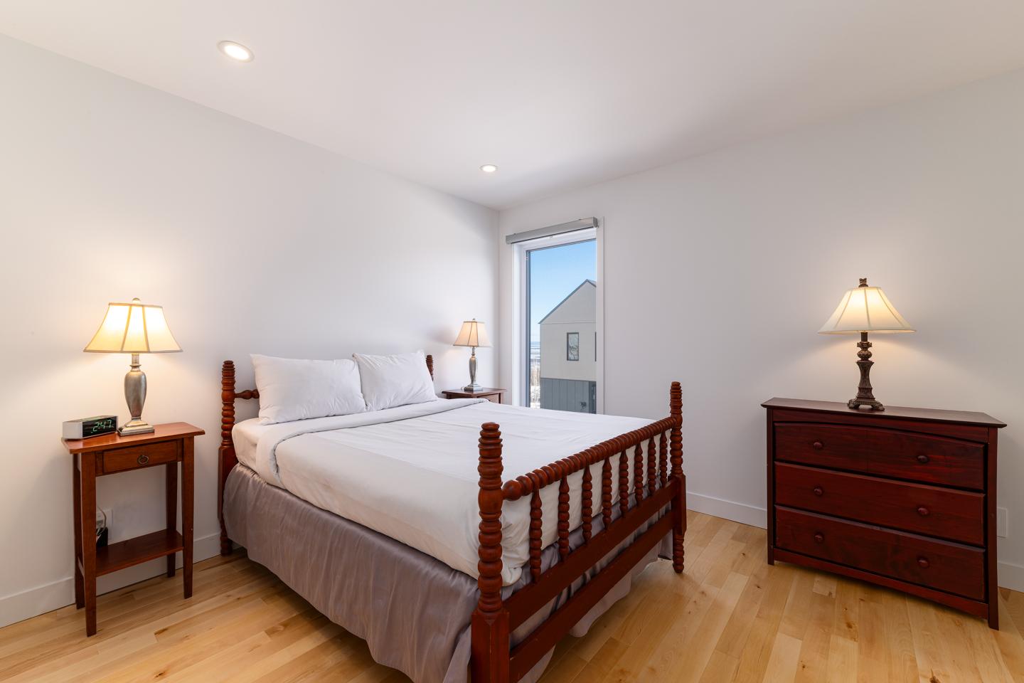 Chambre lumineuse avec lit en bois, lampes et commode.
