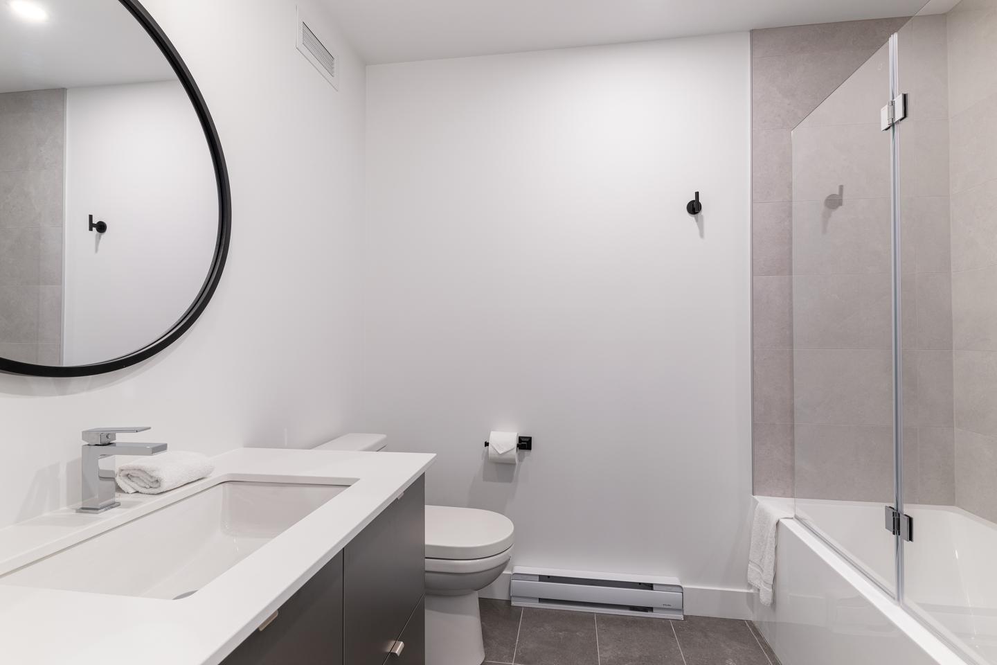 Salle de bain moderne avec baignoire, lavabo et miroir rond.