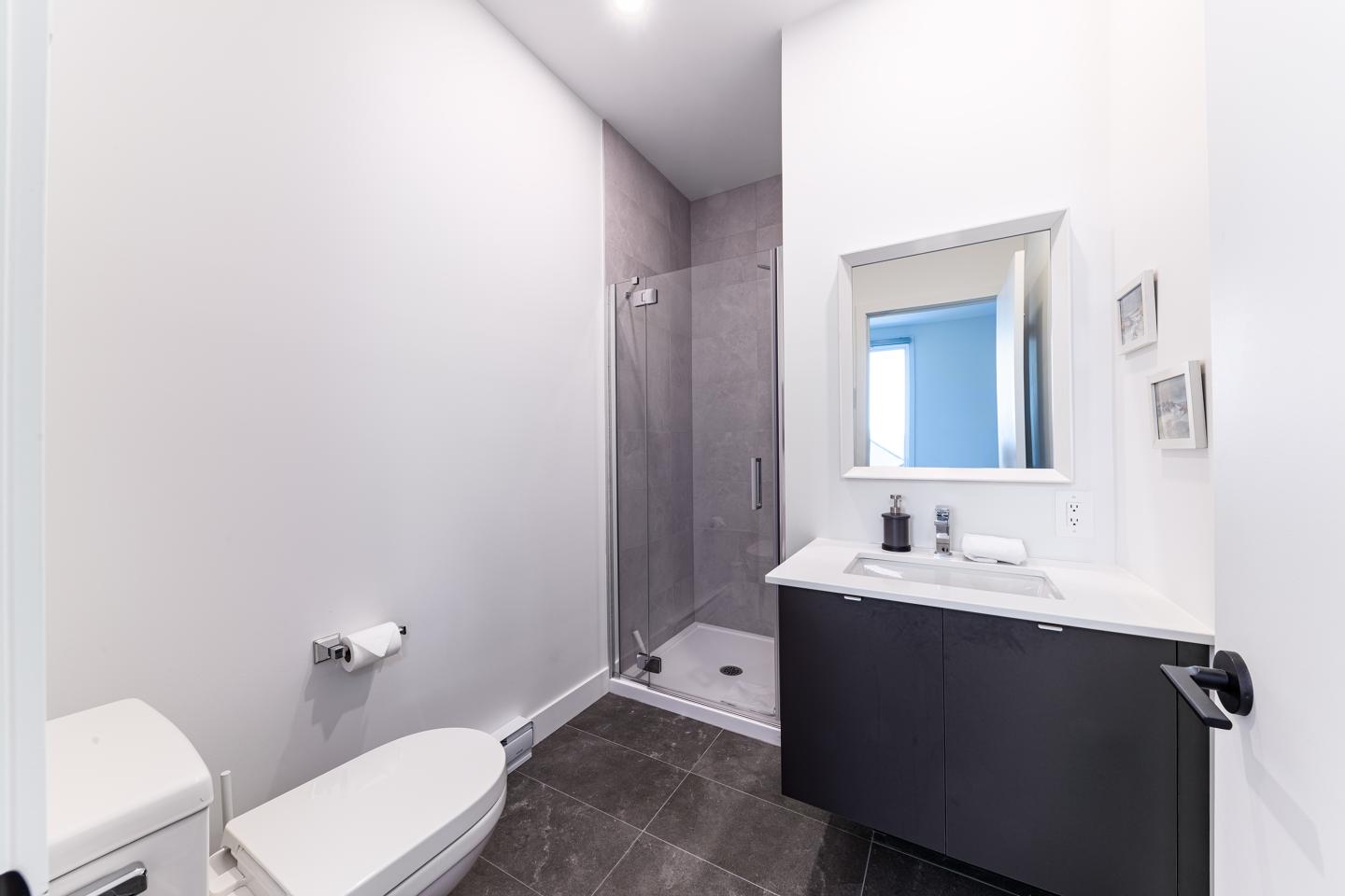 Salle de bain moderne avec douche, lavabo noir et toilettes.