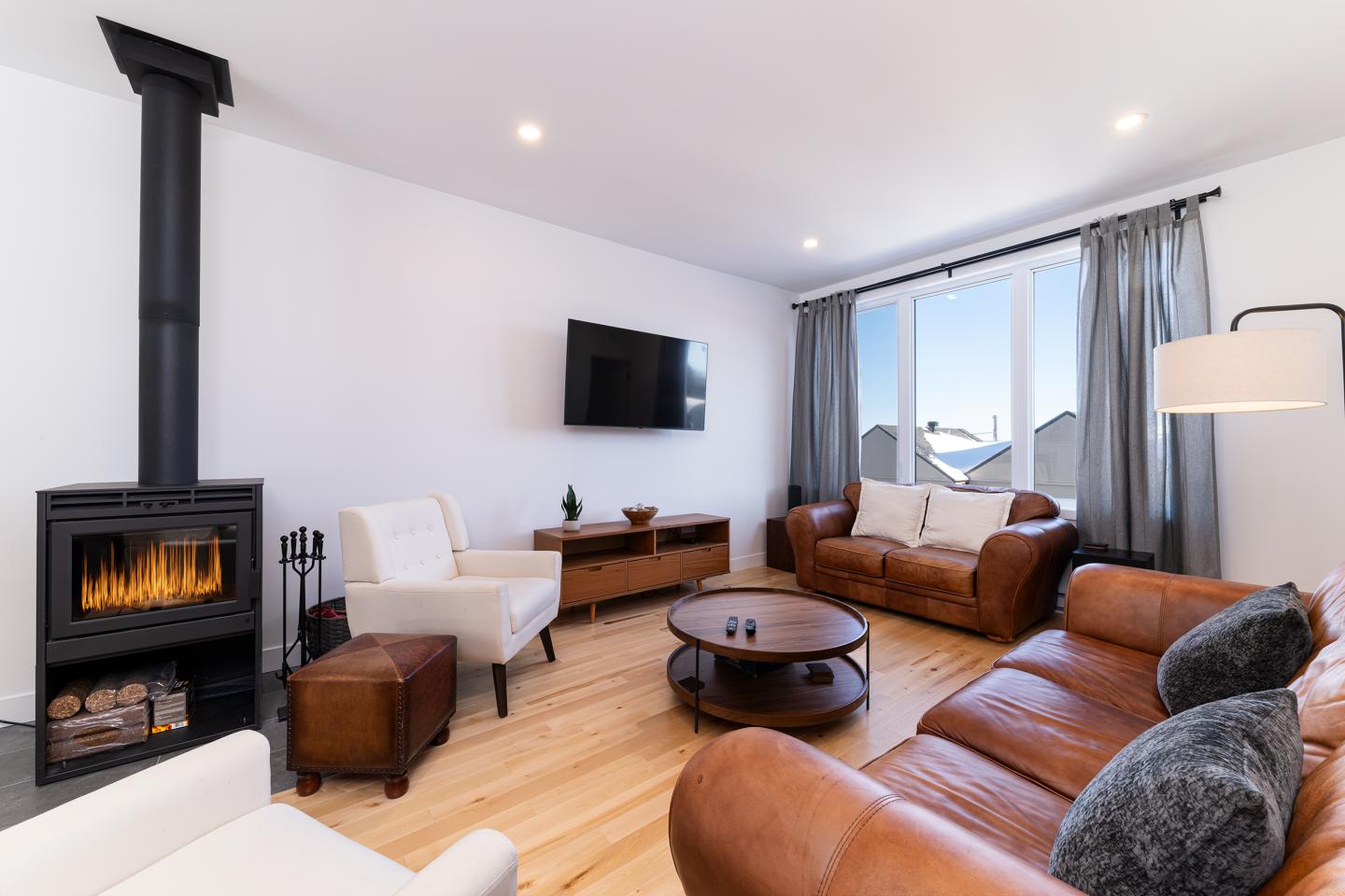 Salon moderne avec canapé en cuir, cheminée et grande fenêtre.