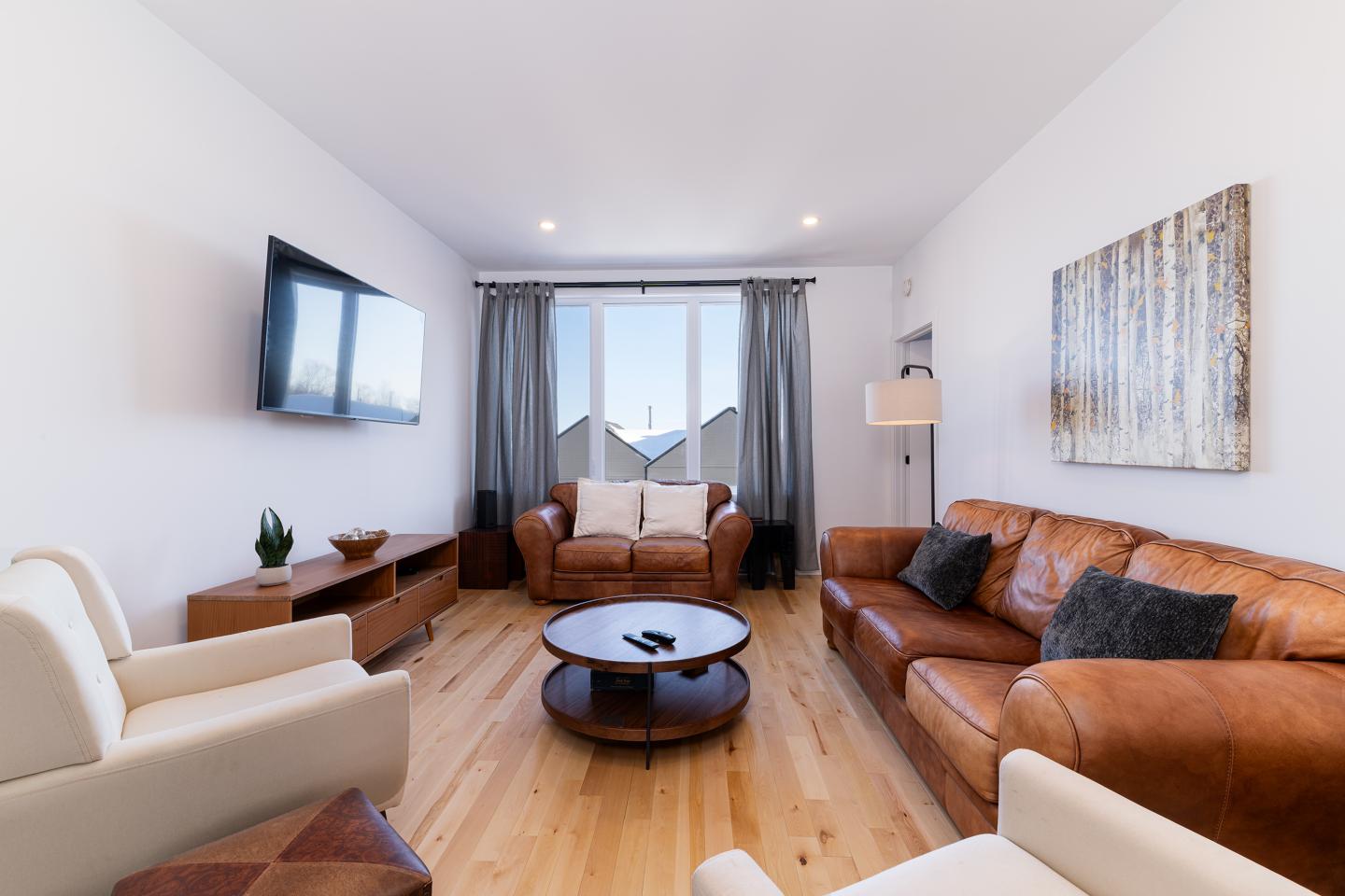 Salon moderne avec canapé en cuir, fauteuils, télévision et table basse en bois.