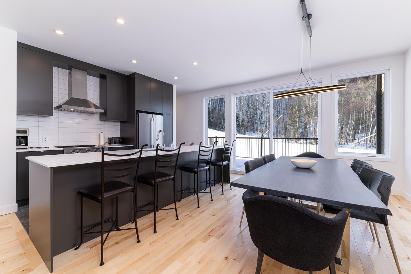 Cuisine moderne avec des armoires noires, îlot central et grande table à manger.