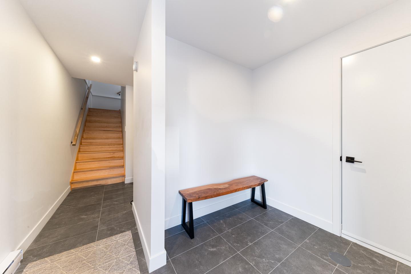 Couloir moderne avec banc en bois, escaliers à gauche.
