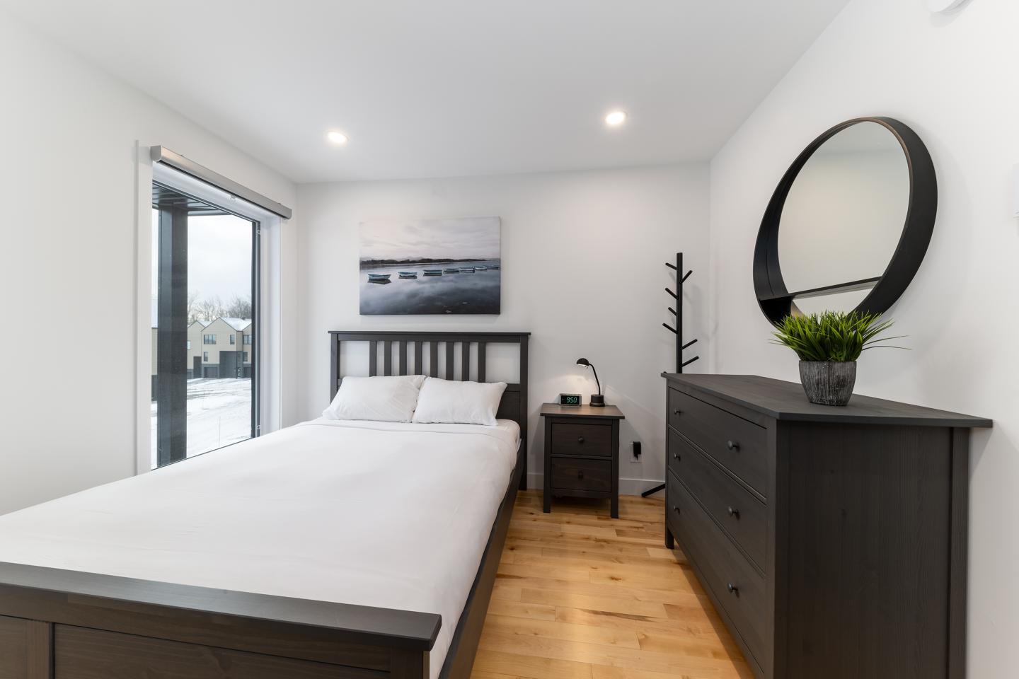 Chambre moderne avec lit, commode noire, miroir rond et plante verte.