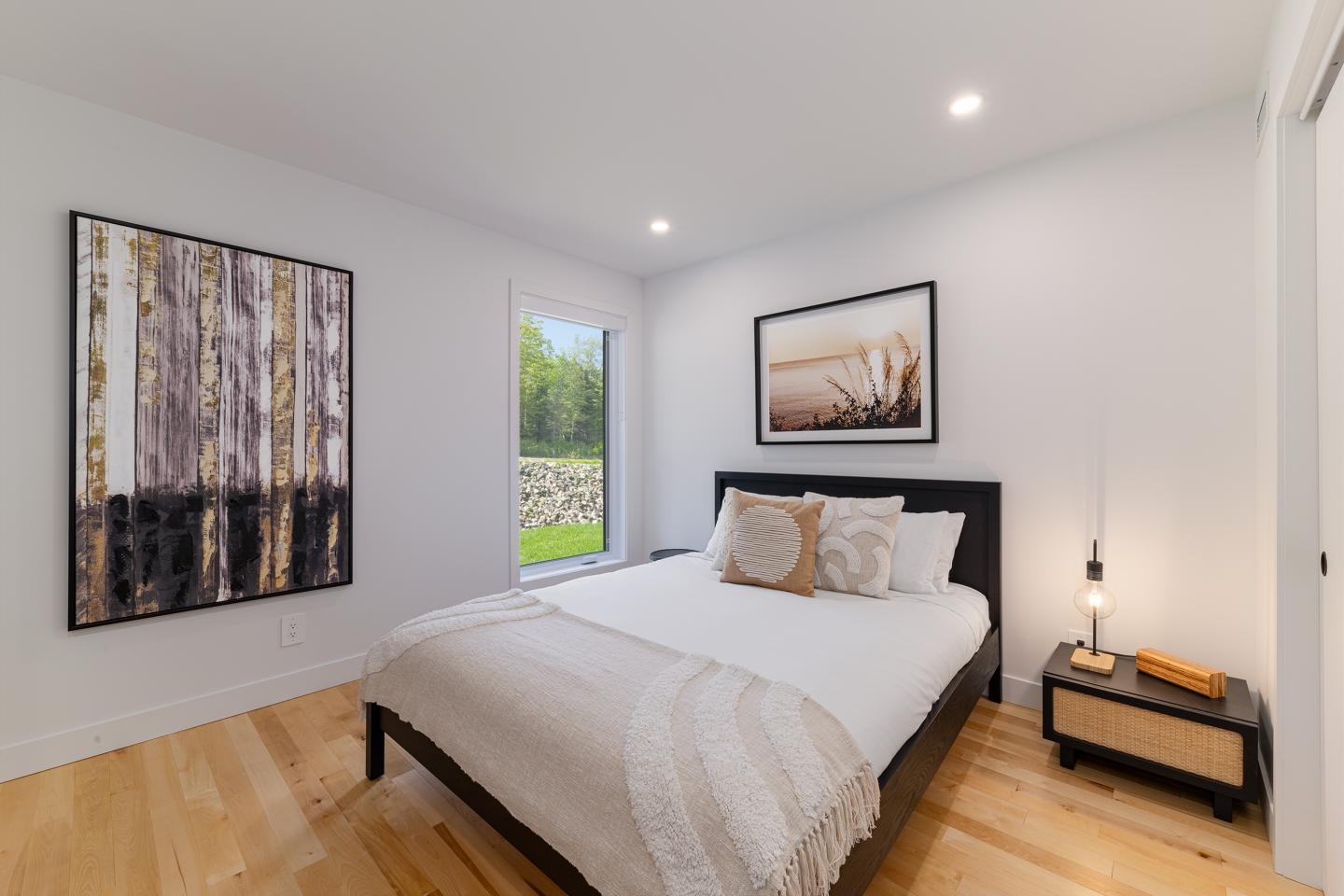 Chambre moderne avec lit double, tableaux muraux, lampe de chevet, grande fenêtre.