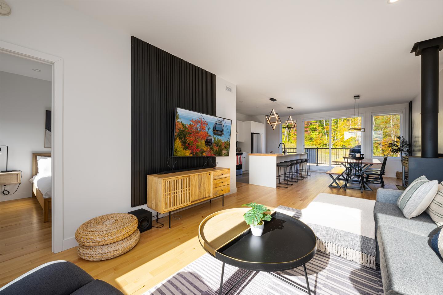 Intérieur moderne et lumineux avec salon et cuisine ouverte, télé allumée, grande fenêtre.