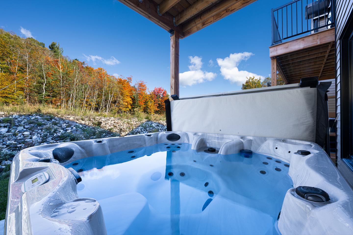 Spa extérieur avec vue sur forêt automnale et ciel bleu.