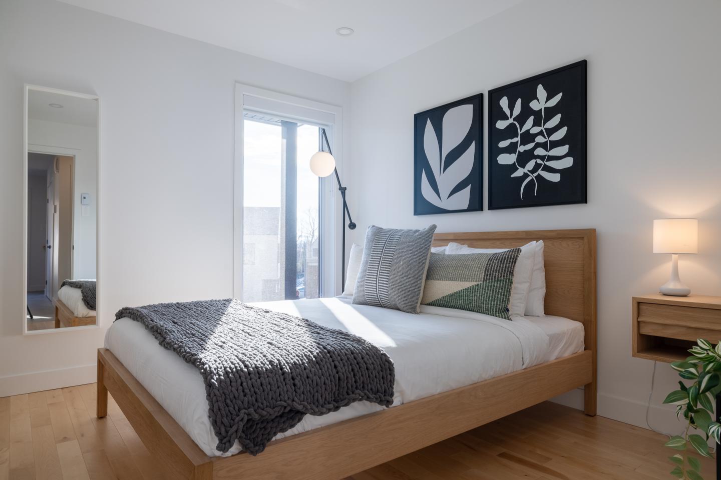 Chambre moderne avec lit en bois, coussins, tableaux noirs et lumière douce.