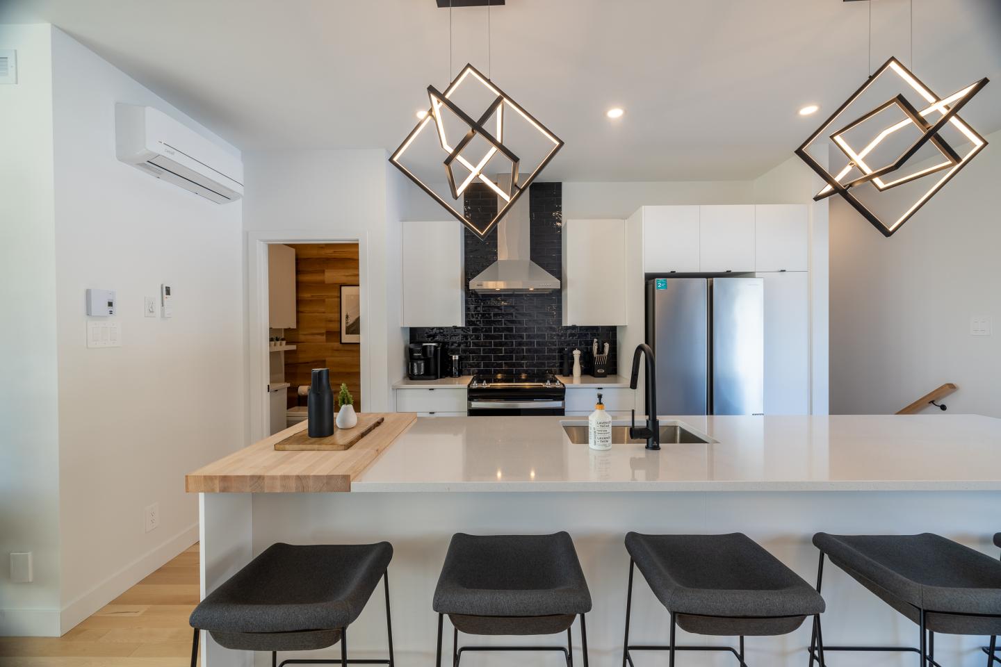 Cuisine moderne avec îlot central, trois tabourets et luminaires géométriques.