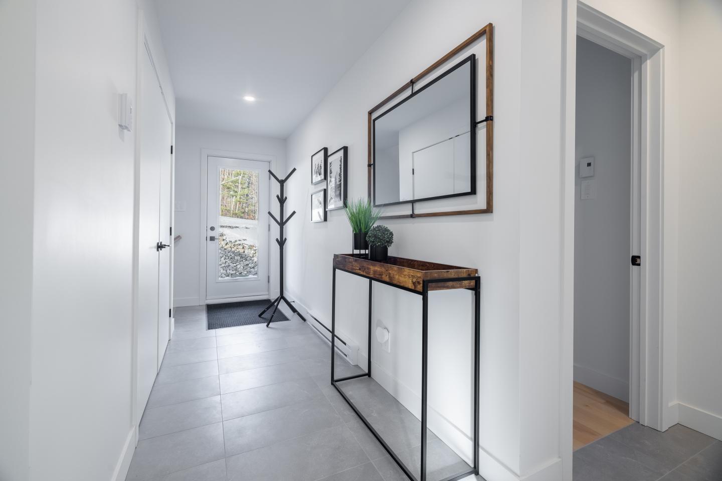 Couloir moderne et lumineux avec miroir, porte-manteau et console en bois.