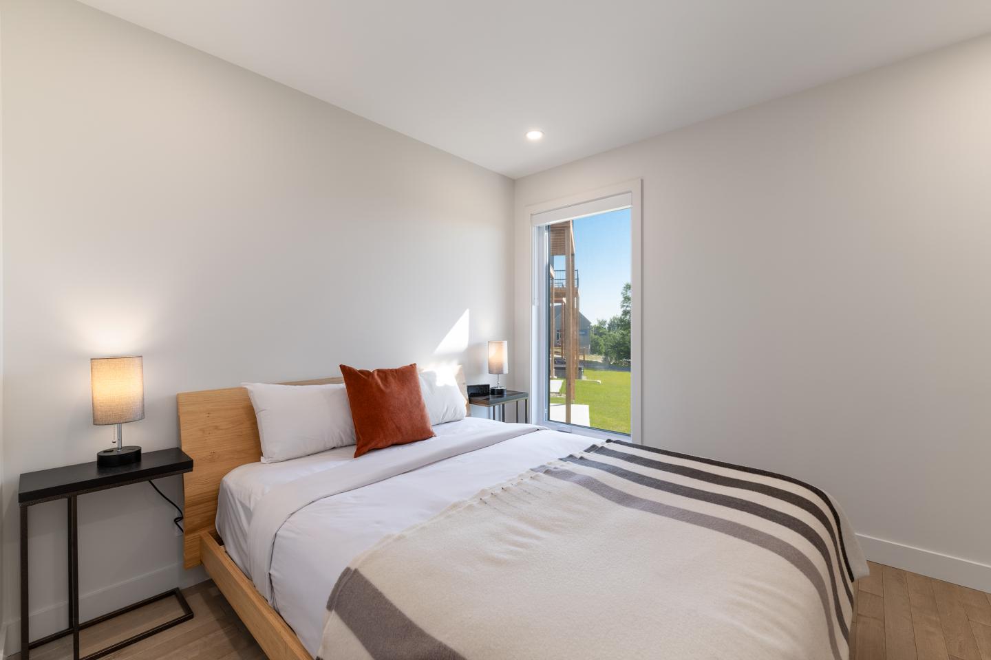 Chambre moderne avec lit double, lampe allumée, porte-fenêtre sur jardin.