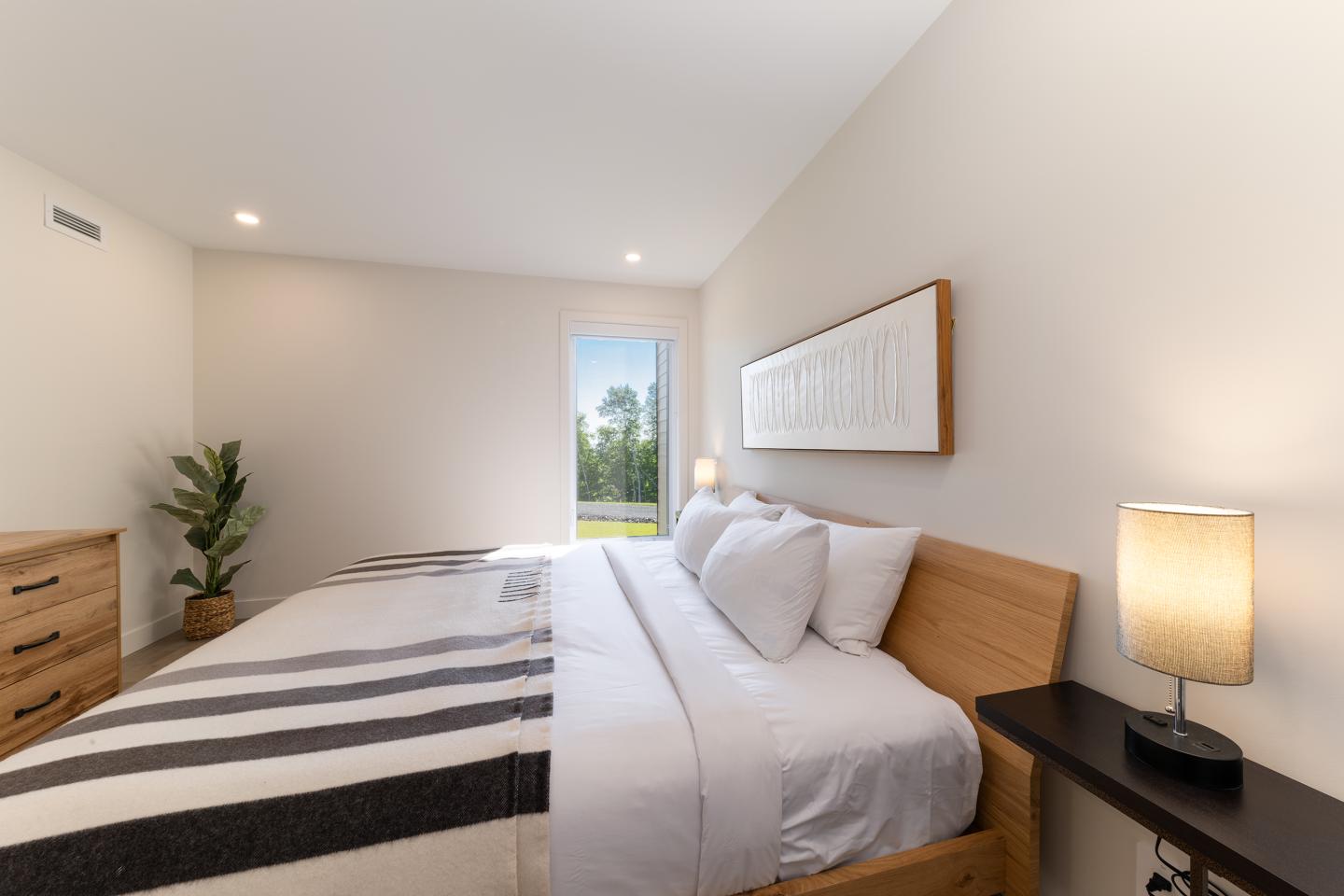 Chambre lumineuse avec lit double, décoration minimaliste, plante et lampe allumée.