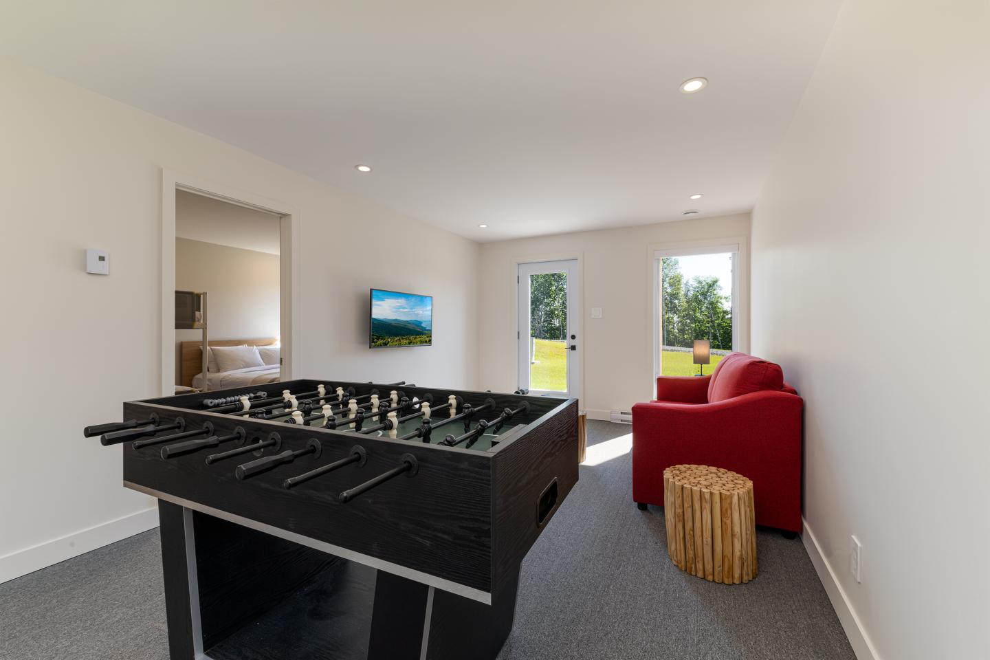 Salle de jeux avec baby-foot, fauteuil rouge et vue sur jardin.