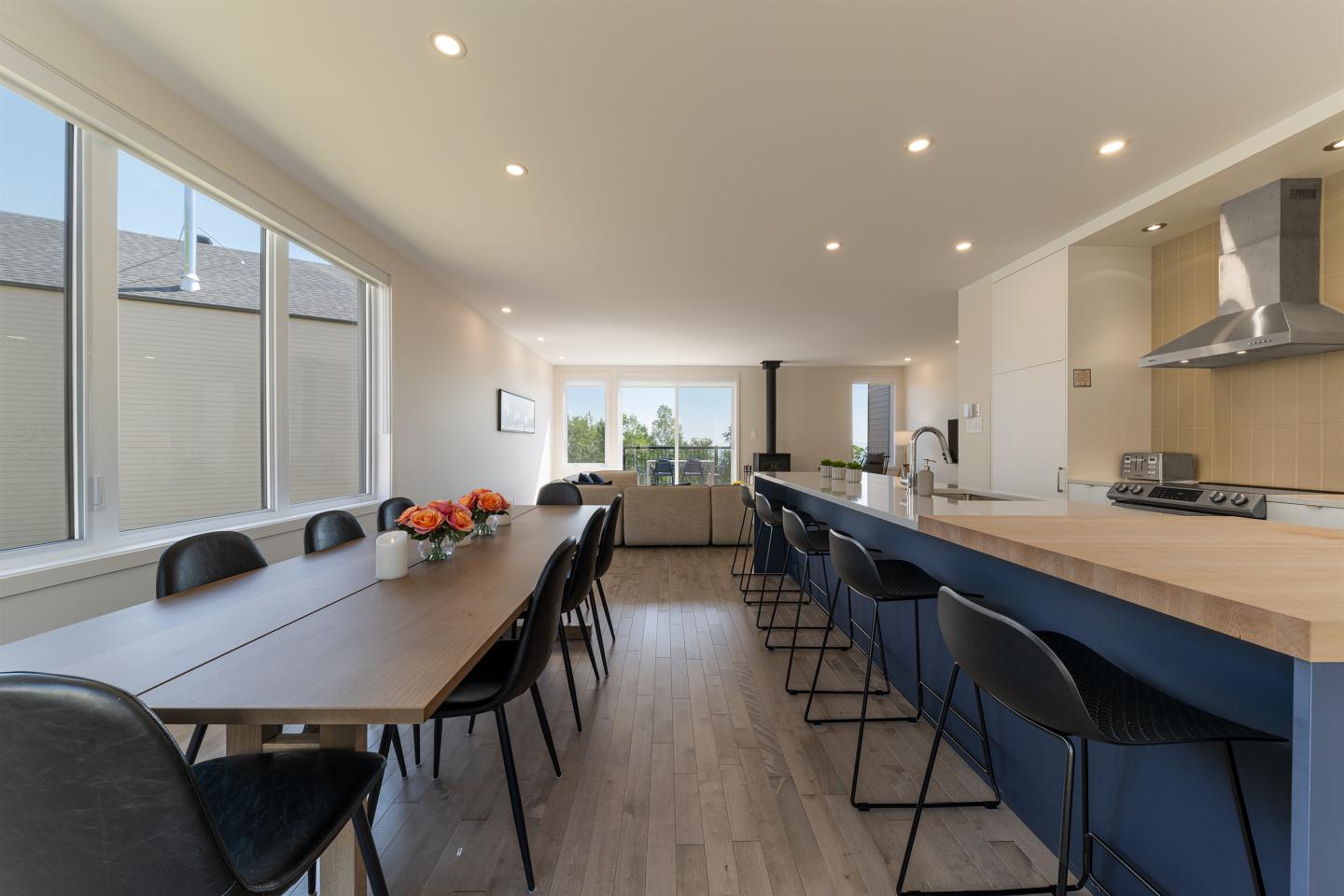 Salle à manger et cuisine modernes, table longue, chaises noires, lumière naturelle.