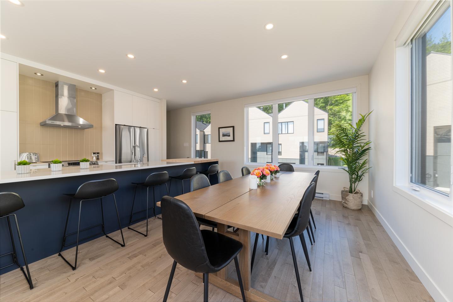 Grande cuisine moderne avec îlot, table en bois et grande fenêtre.