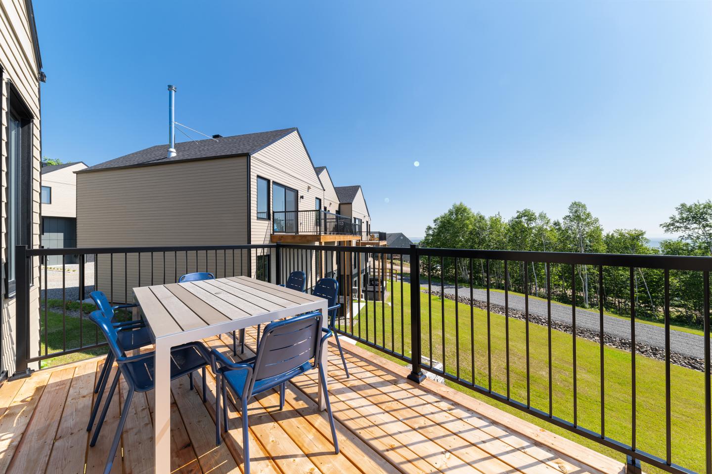 Terrasse ensoleillée avec table, chaises bleues et vue sur jardin et maisons modernes.