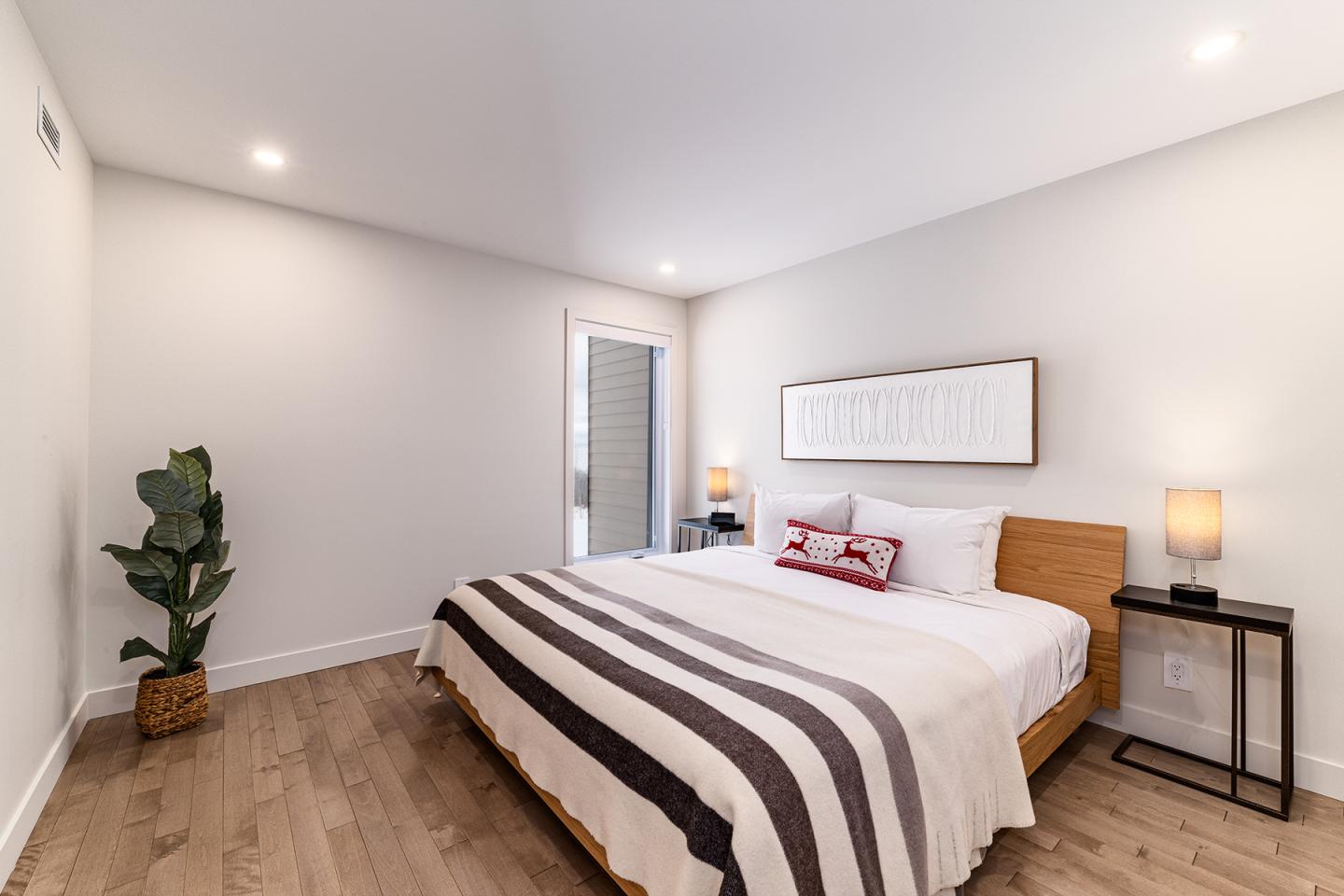 Chambre moderne avec lit, deux lampes et plante dans un coin.