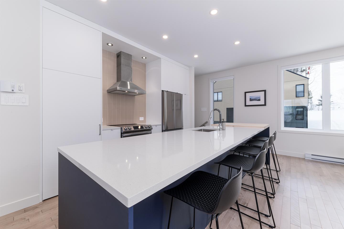 Cuisine moderne blanche avec îlot central et tabourets noirs.