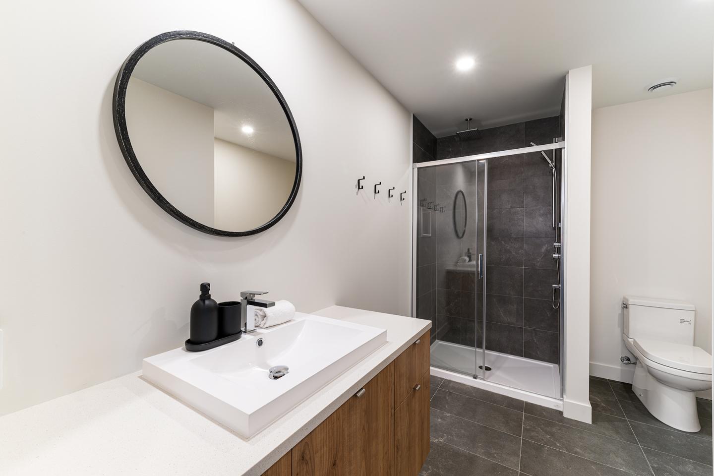 Salle de bains moderne avec lavabo, miroir rond, douche et toilettes.