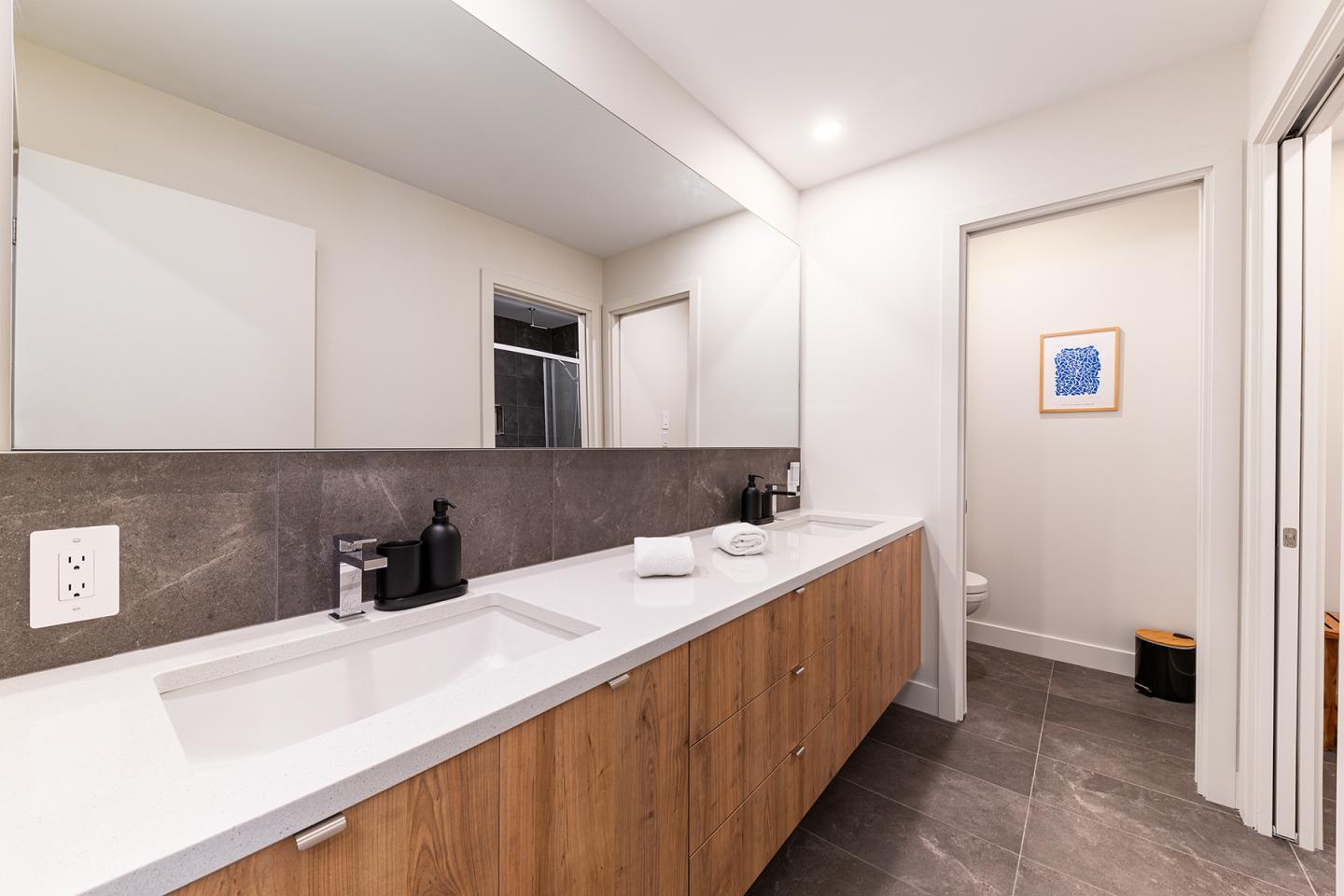 Salle de bain moderne avec lavabo, miroir large et carrelage gris.