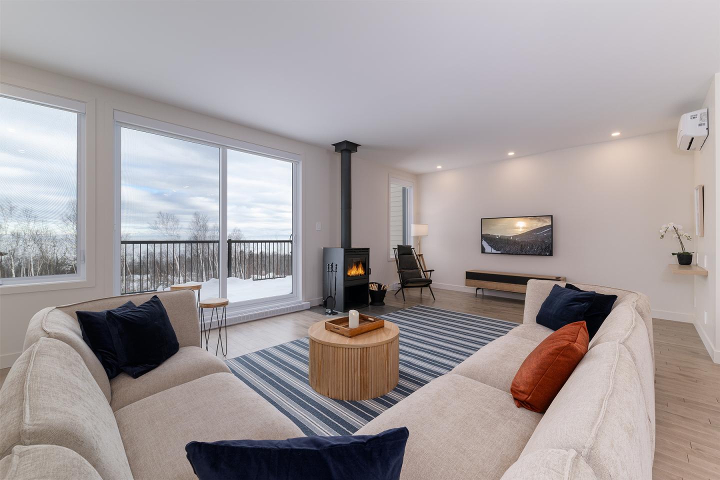 Salon moderne avec canapé beige, cheminée, et TV, vue sur l'extérieur enneigé.