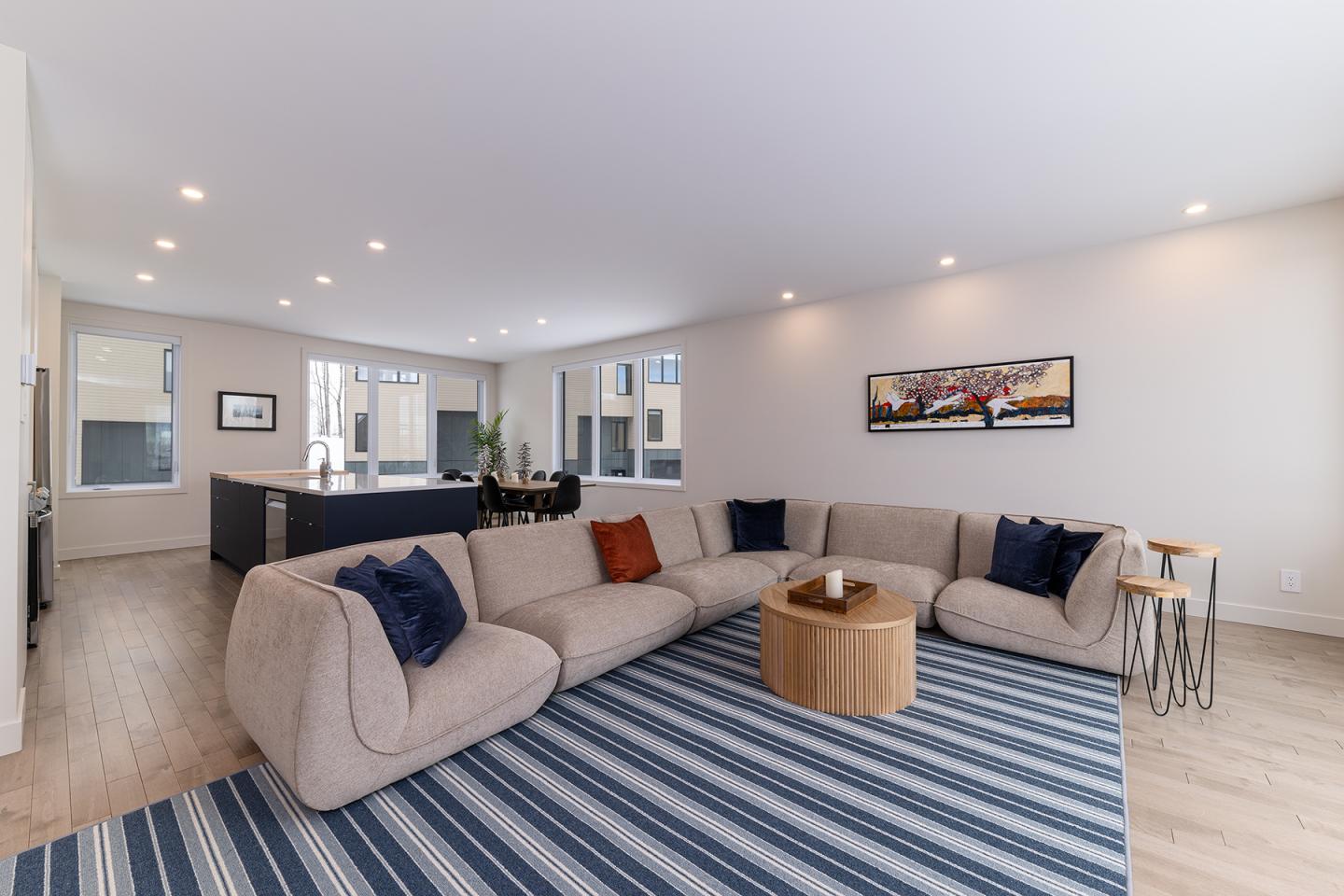 Salon moderne avec canapé beige, tapis bleu rayé et table en bois.