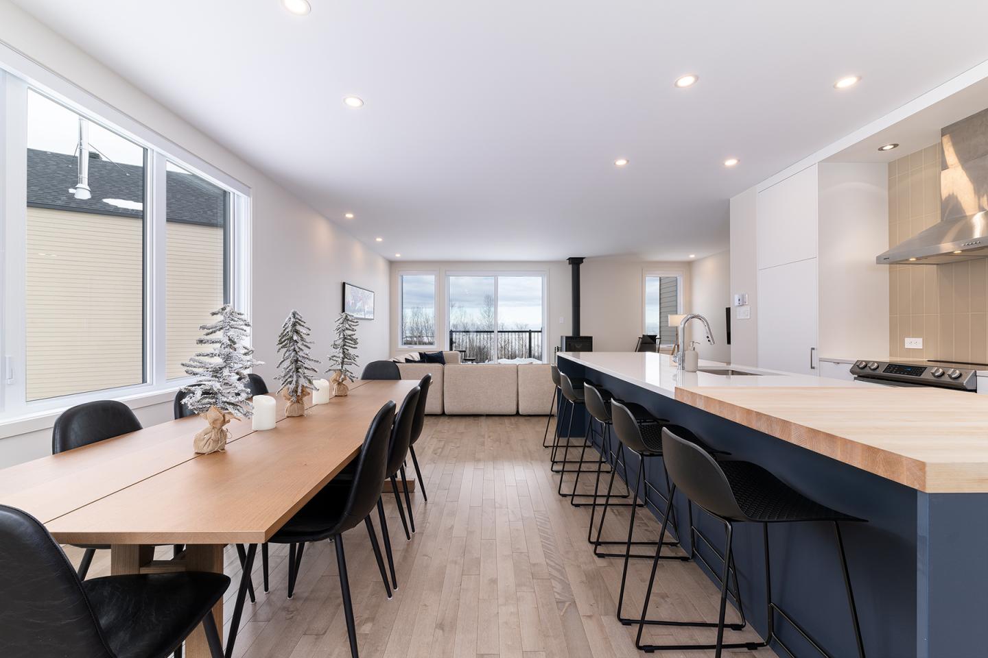 Cuisine moderne et lumineuse avec grand îlot central et table à manger en bois.