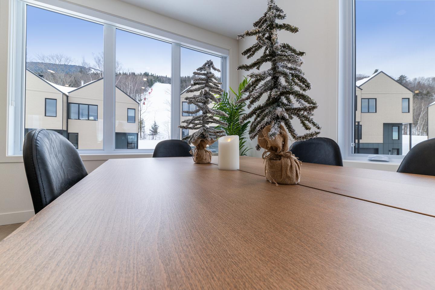 Table en bois avec décorations d'arbres enneigés, grandes fenêtres, extérieur enneigé.