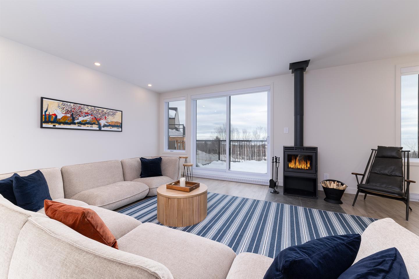 Salon moderne avec cheminée, canapé beige, et vue sur balcon enneigé.