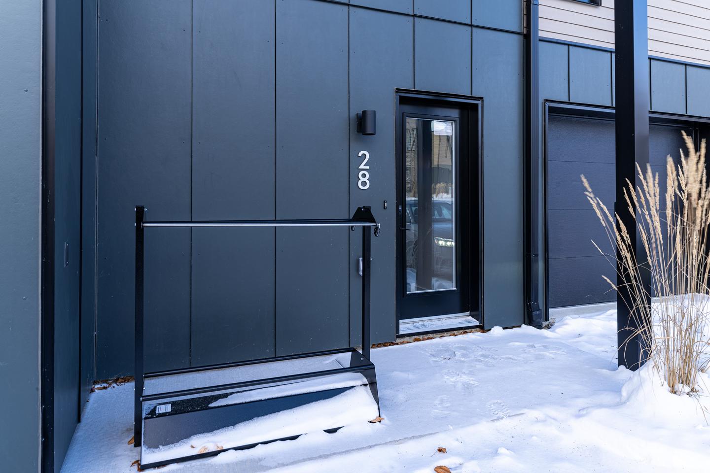 Entrée enneigée d'un bâtiment moderne, numéro 28, avec graminées à droite.