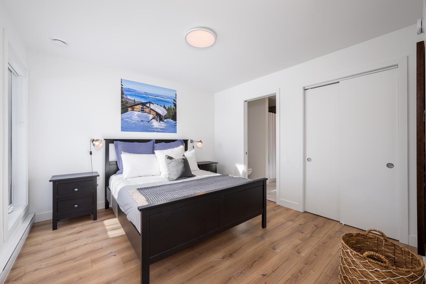 Chambre moderne avec lit double noir et tableau mural, parquet clair.