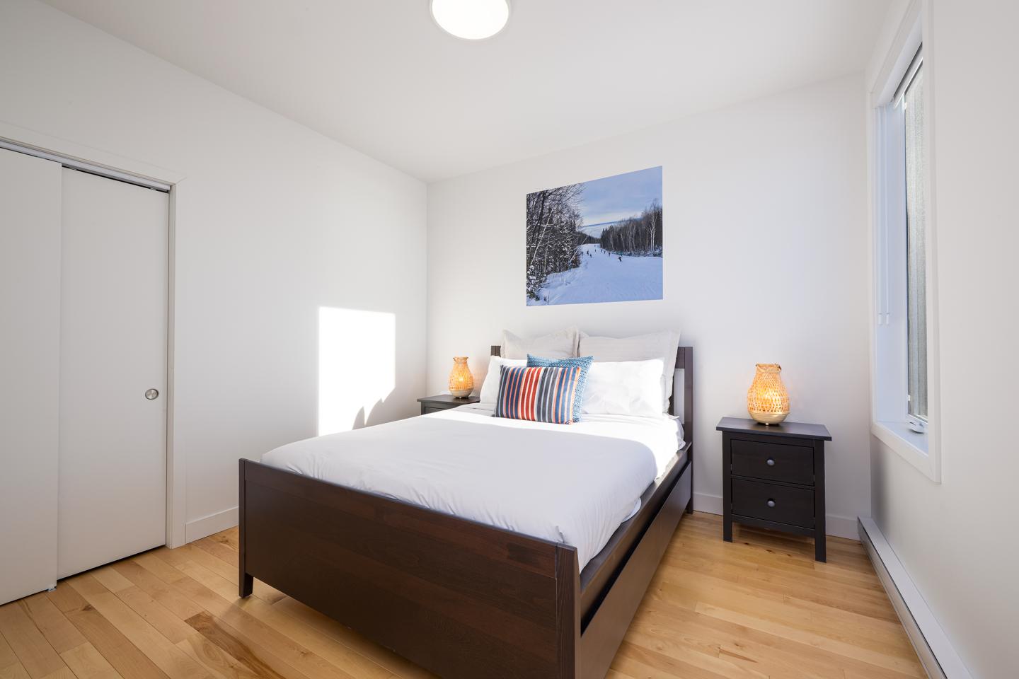 Chambre lumineuse avec lit double, deux tables de chevet et tableau au mur.
