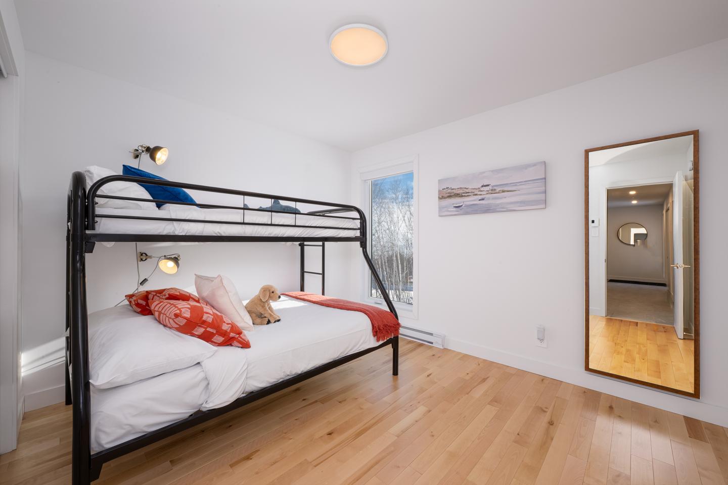 Chambre blanche avec lit superposé, miroir et parquet en bois.