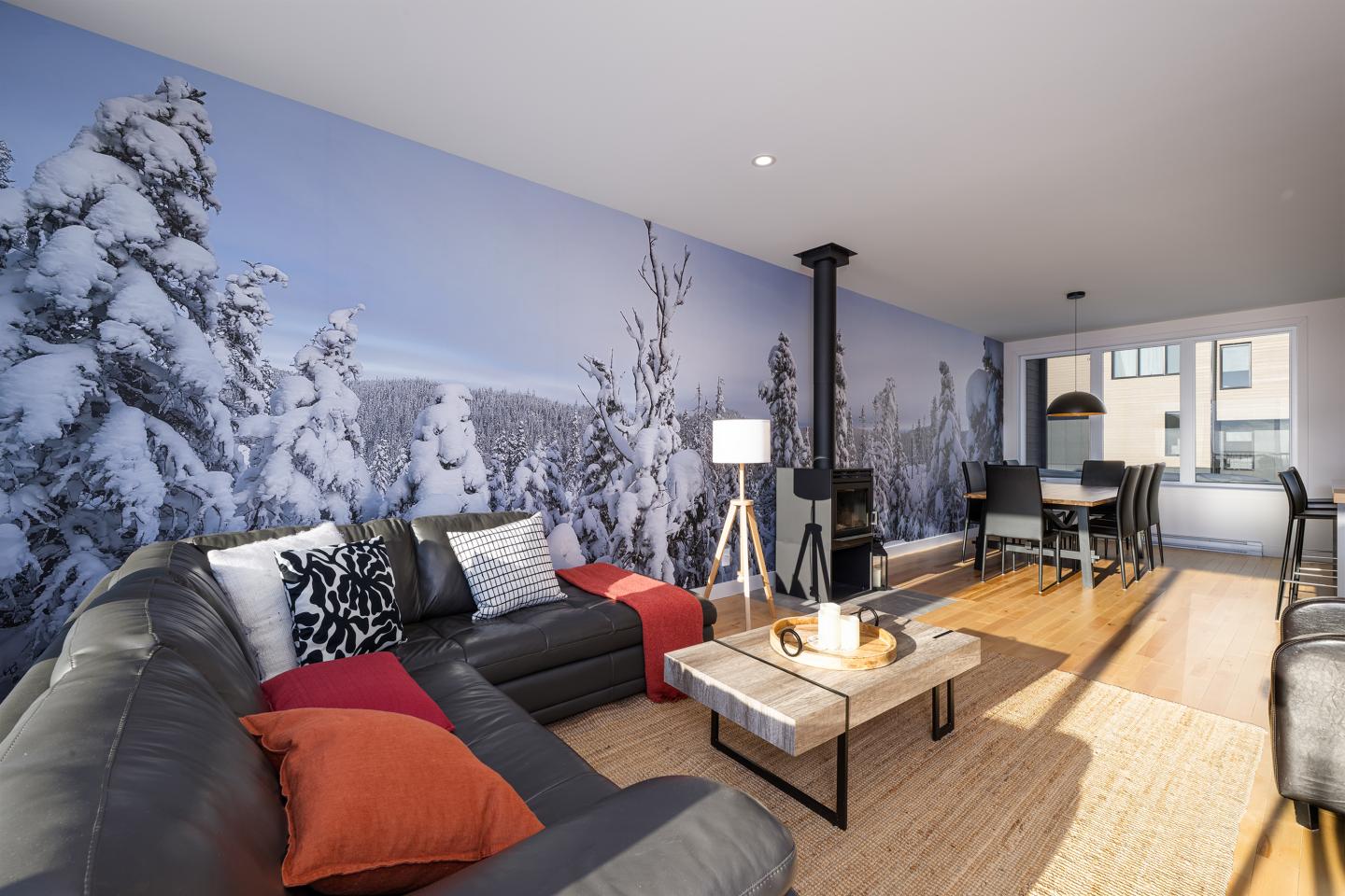 Salon moderne avec canapé gris, cheminée et mur décoré d'une fresque enneigée.