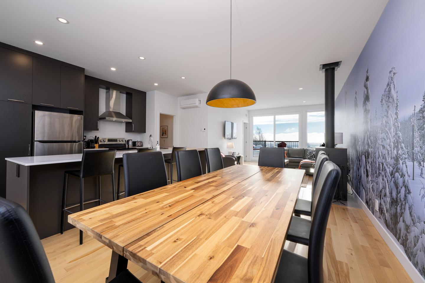 Salle à manger moderne, table en bois, chaises noires, cuisine en arrière-plan.