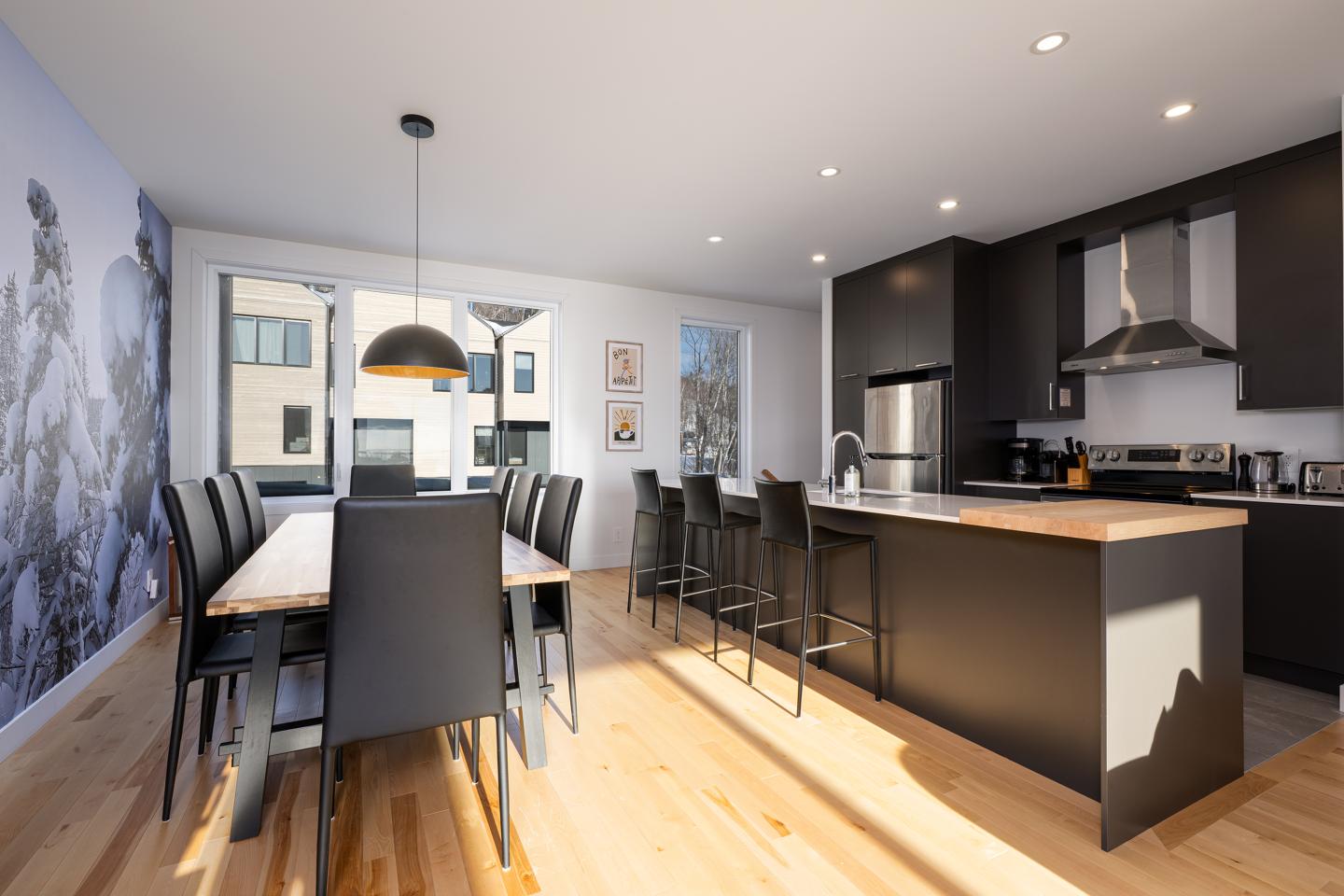 Cuisine moderne avec table en bois, chaises noires, et îlot central.