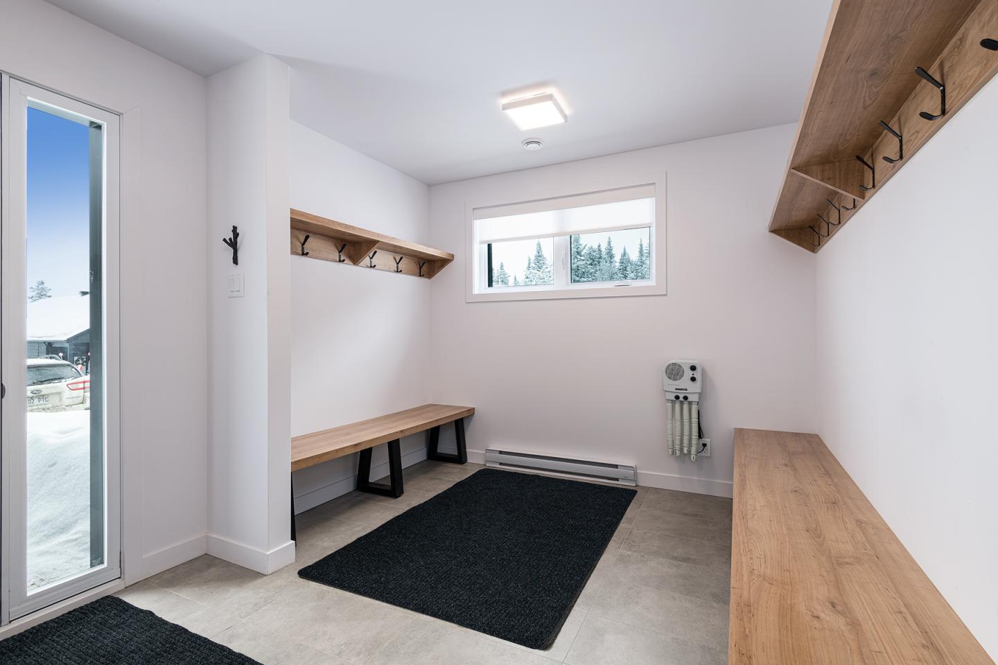 Vestiaire moderne avec bancs en bois, crochets et fenêtre, lumière naturelle.