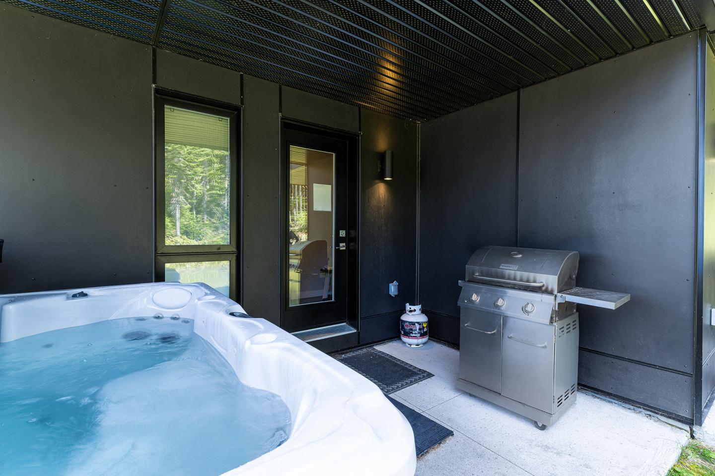 Spa extérieur avec barbecue en acier inoxydable sur terrasse couverte.