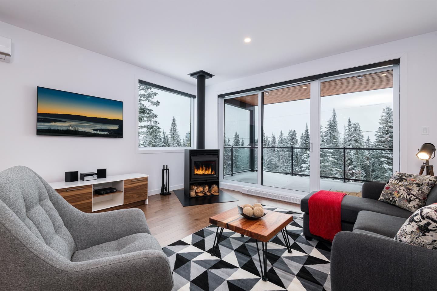 Salon moderne avec vue sur la neige, cheminée et canapé confortable.
