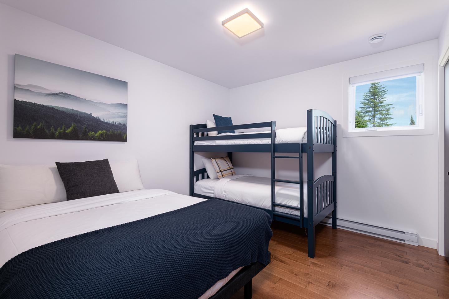 Chambre avec lit double, lits superposés, tableau mural et fenêtre.