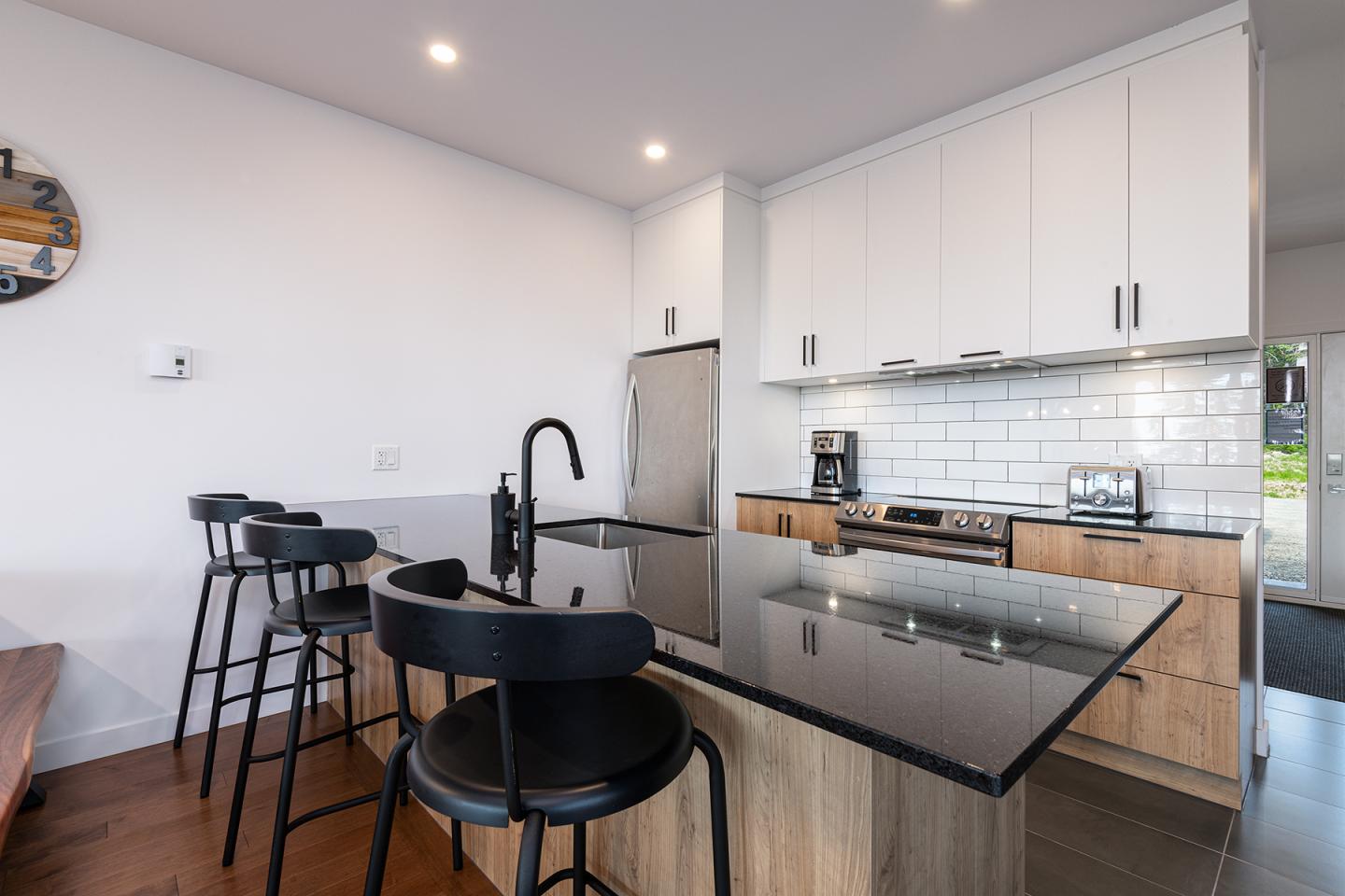 Cuisine moderne avec un îlot central, chaises noires et des armoires blanches.