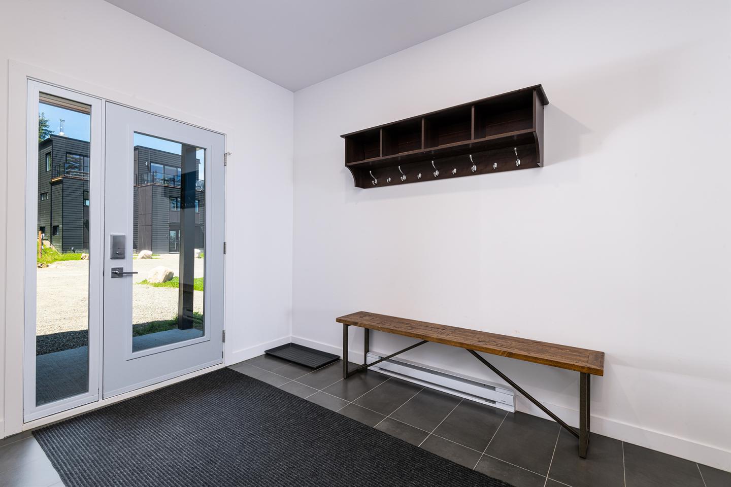 Entrée avec banc en bois, porte vitrée et étagère murale.