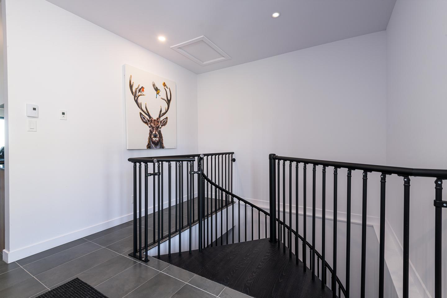 Escalier avec rambarde noire, tableau de cerf sur mur blanc.