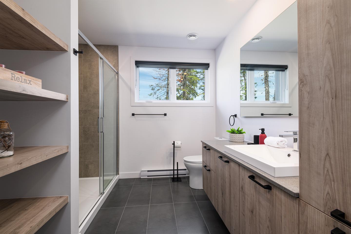 Salle de bain moderne avec douche en verre, lavabo double et fenêtre éclairée.