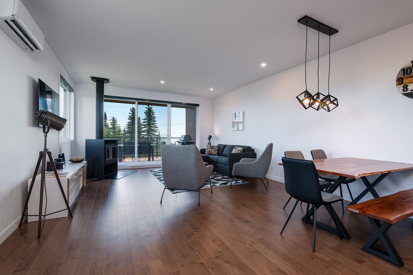 Salon moderne avec parquet, canapé gris et table en bois. Fenêtres sur balcon avec vue.