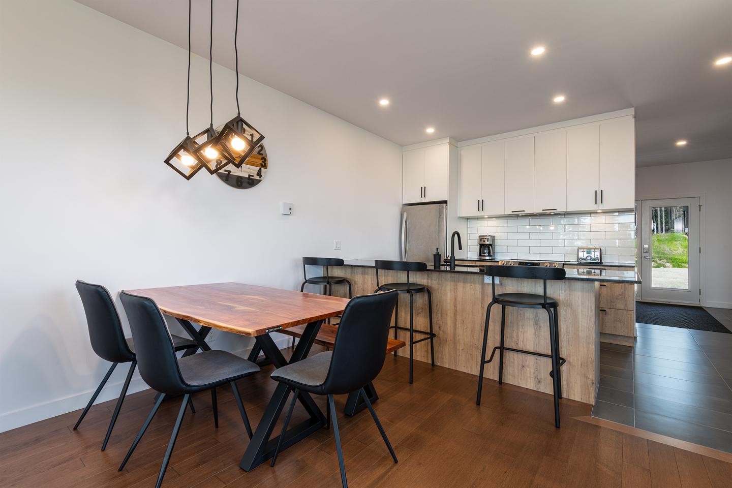 Salle à manger moderne avec table en bois, chaises noires et cuisine ouverte.