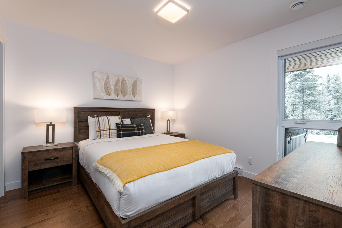Chambre moderne avec lit double, couette jaune, deux lampes et fenêtre donnant sur l'extérieur.