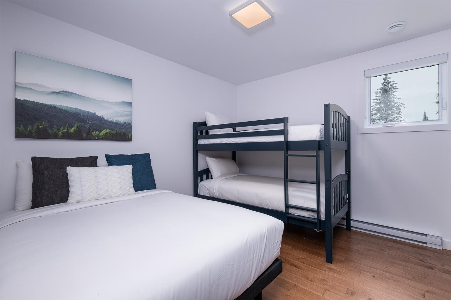 Chambre avec lit double et lits superposés, mur blanc, tableau paysage.