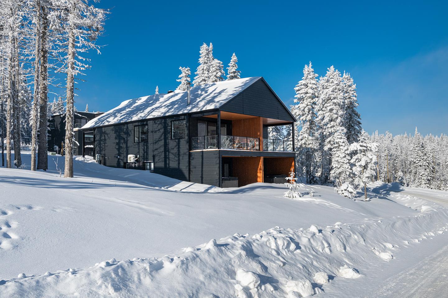 Chalet moderne en bois entouré de neige, ciel bleu clair.
